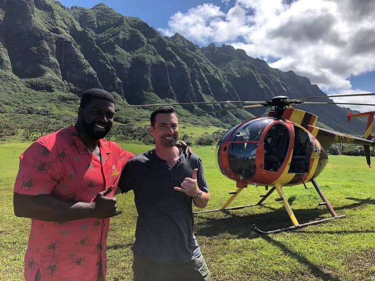 Two guests posing next to a helicopter at a private mountain landing site on Oahu