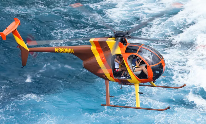 View from inside a doors-off helicopter showing open cabin and coastline